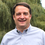 Smiling man with brown hair and collared shirt.
