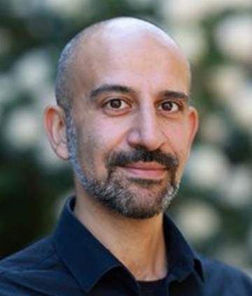 A brown eyed middle aged man, with facial hair and cropped gray-black hair, looking at camera with a pleasant expression.